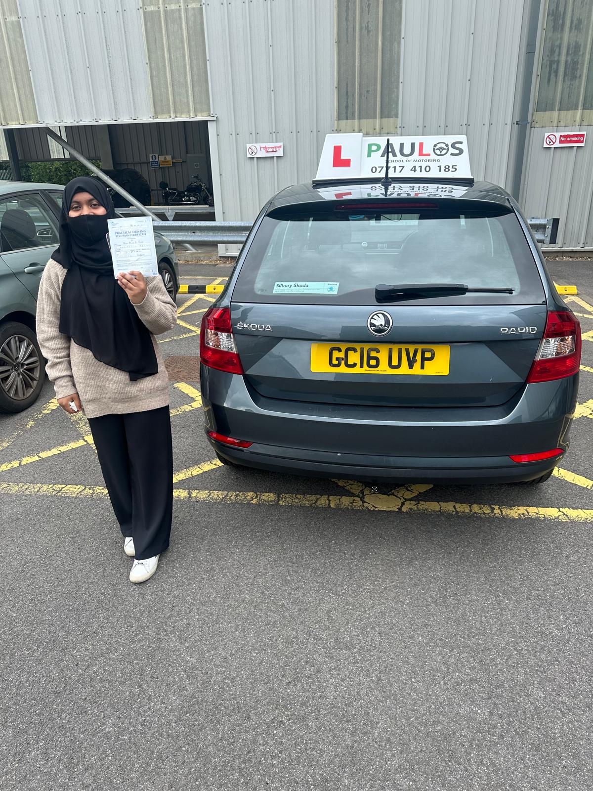 Pupil holding her practical driving test pass certificate beside a Paulos car