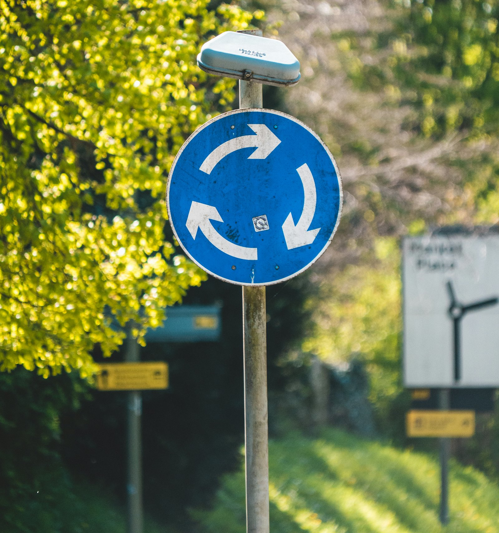 A blue mini-roundabout sign beside a British country road