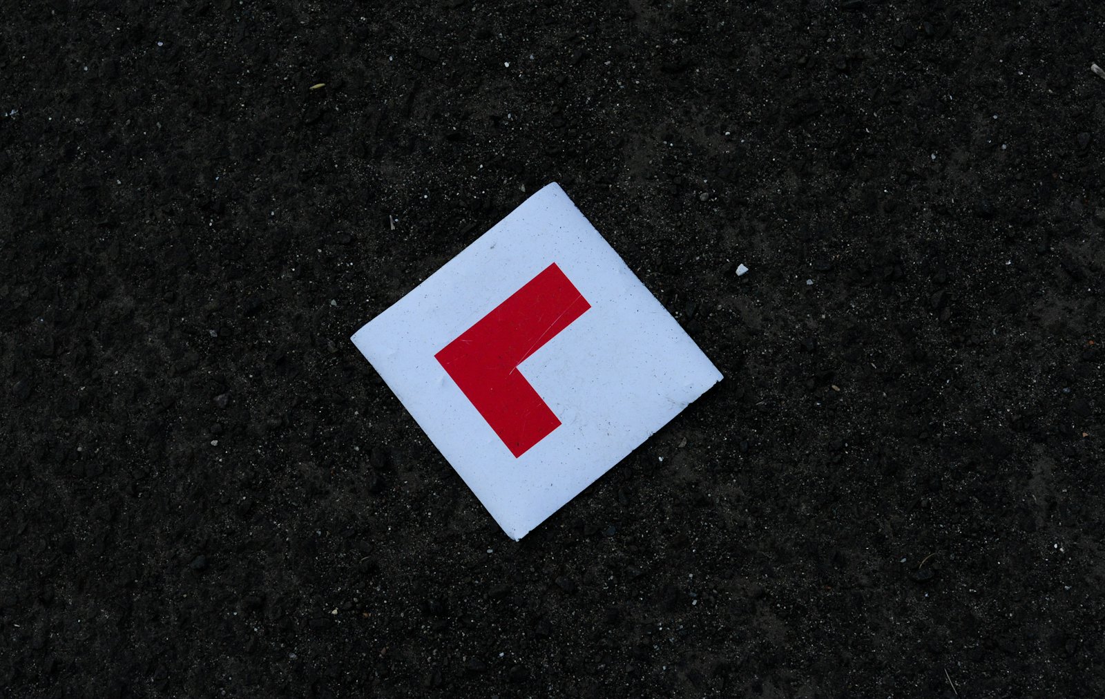 A red L plate lying on asphalt