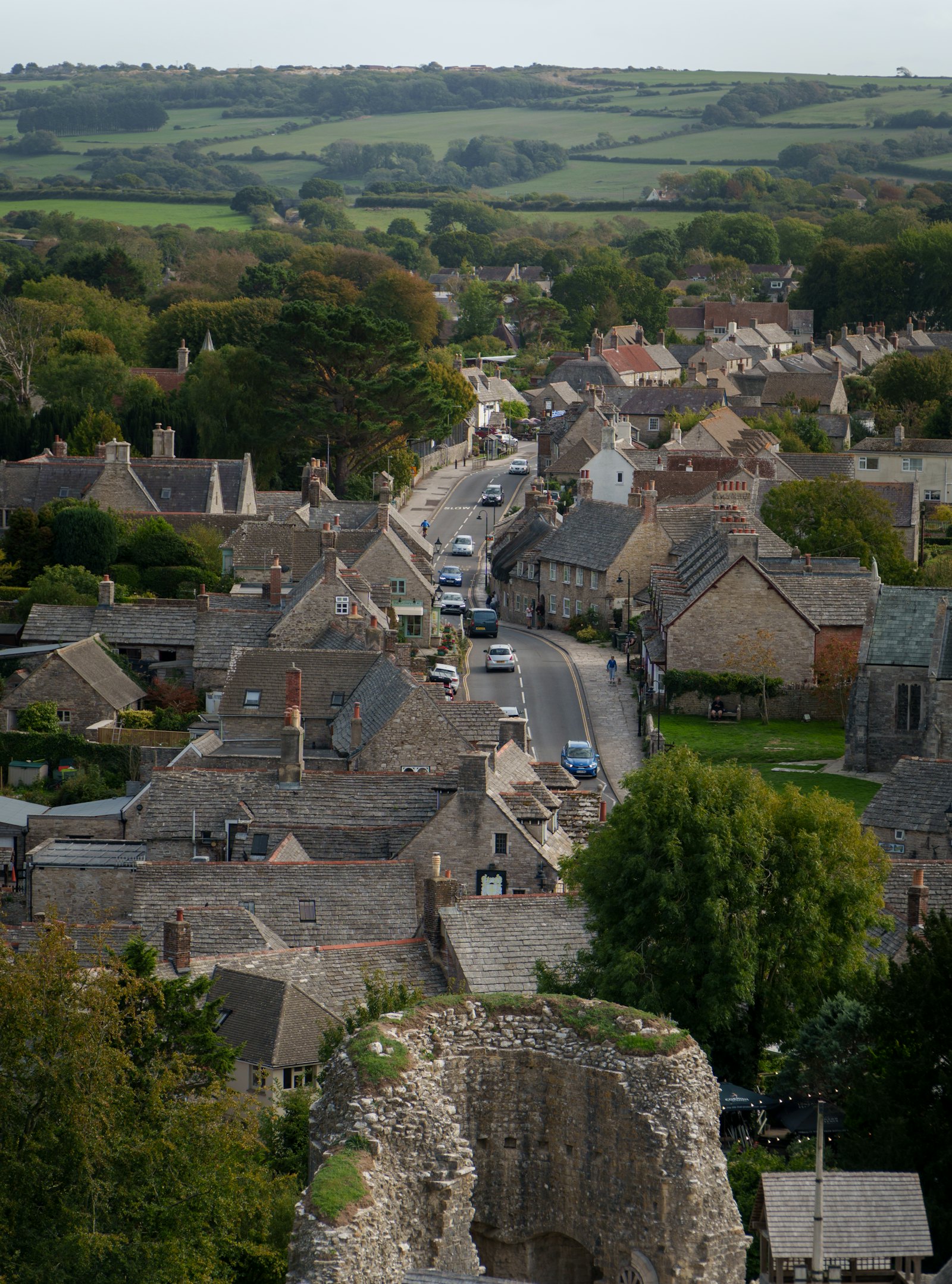 A road through a stone village, with green hills beyond